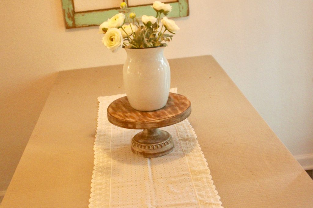 a vintage lace table runner with an enamelware vase