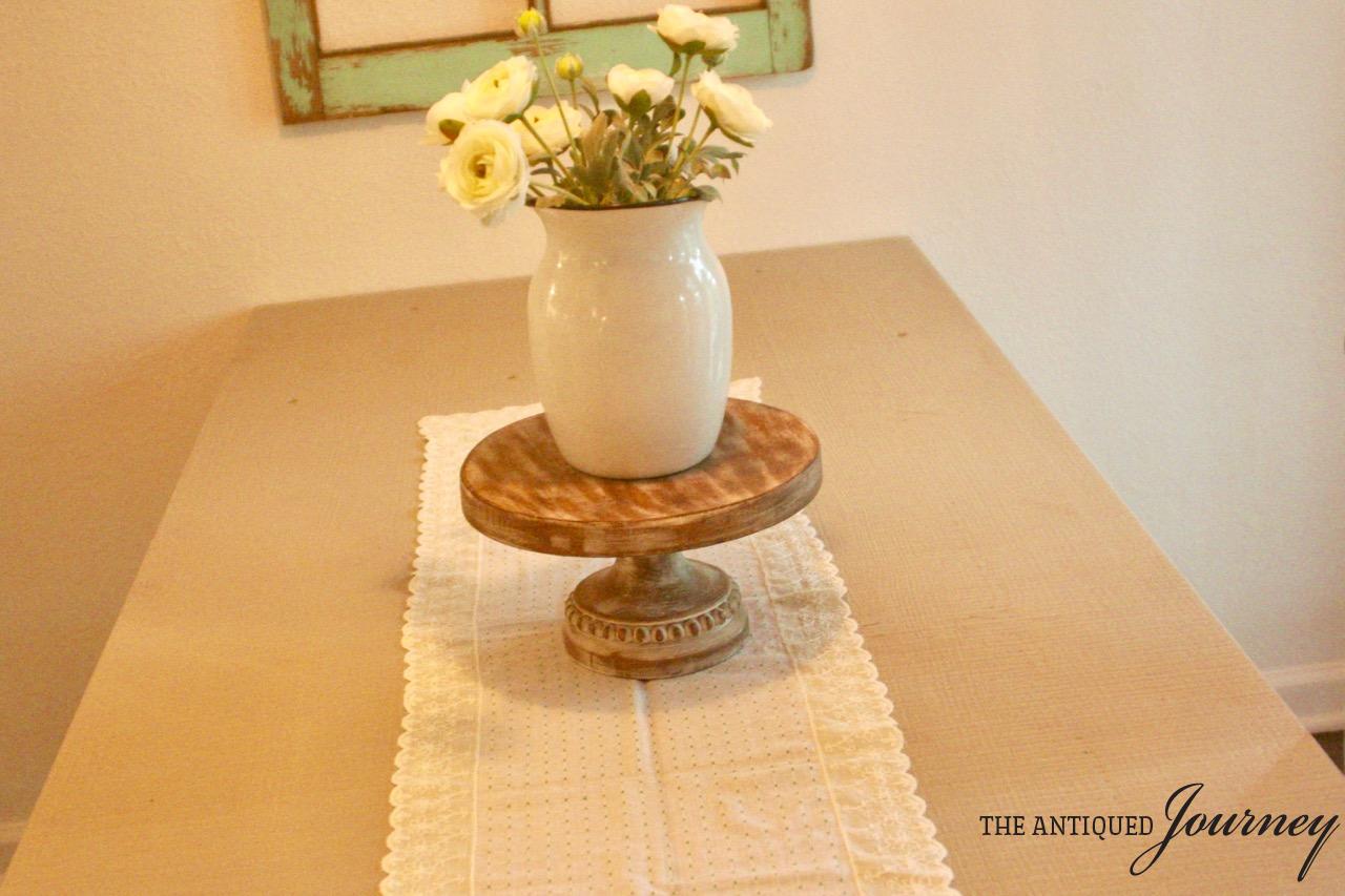 a vintage lace table runner with an enamelware vase