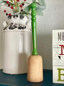 a vintage wooden masher with a green handle