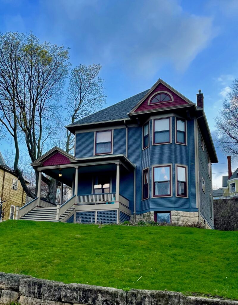 a blue and purple Queen Anne style Victorian house on a hill