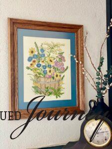 a floral needlework picture in a wood frame hung next to a fireplace