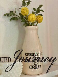 a vintage pottery 'cream' bottle filled with yellow faux stems