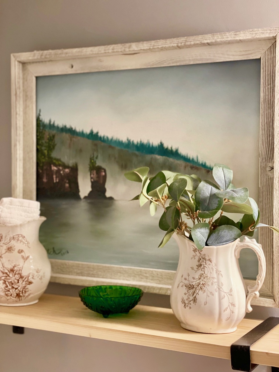 a modern wooden shelf disaplayed with antique transferware pitchers pairs nicely with a modern oil painting behind them