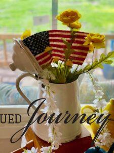 a vintage white enamel pitcher filled with faux yellow stems and a flag
