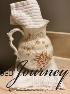 an antique transferware pitcher holds a towel in a bathroom