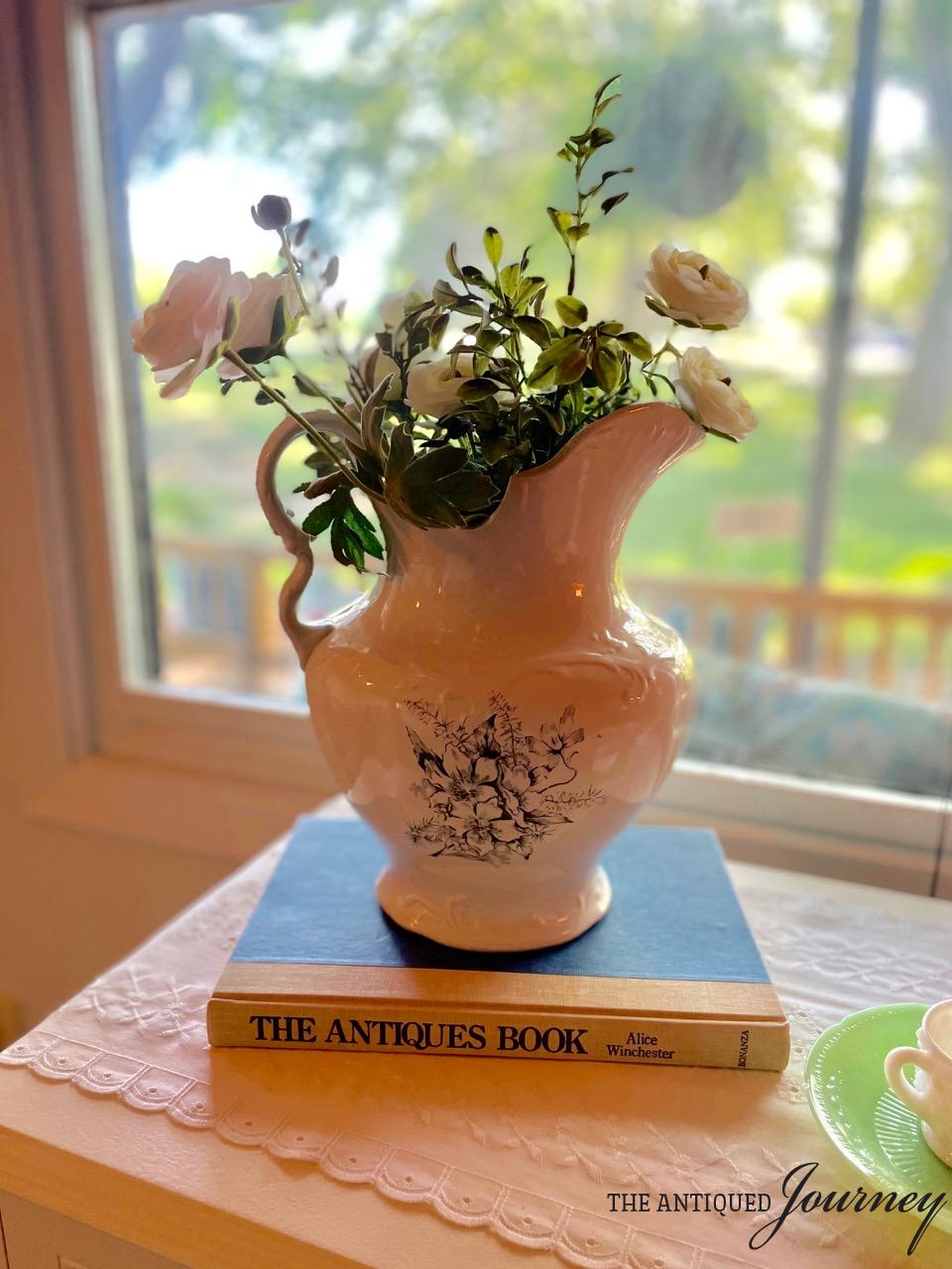 an antique transferware pitcher displayed on top of a vintage book