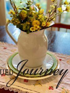 a stack of vintage plates underneath an enamel pitcher filled with flowers