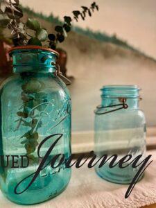 vintage blue jars with faux eucalyptus displayed on a bathroom shelf with a vintage linen