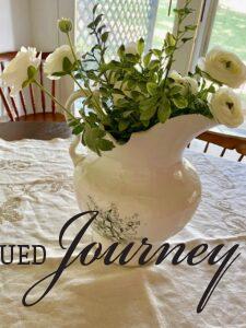 an antique pitcher filled with faux white flowers on a vintage linen