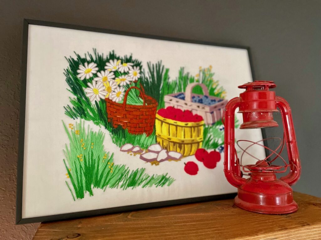a vintage crewelwork art picture displayed with an antique railroad lantern