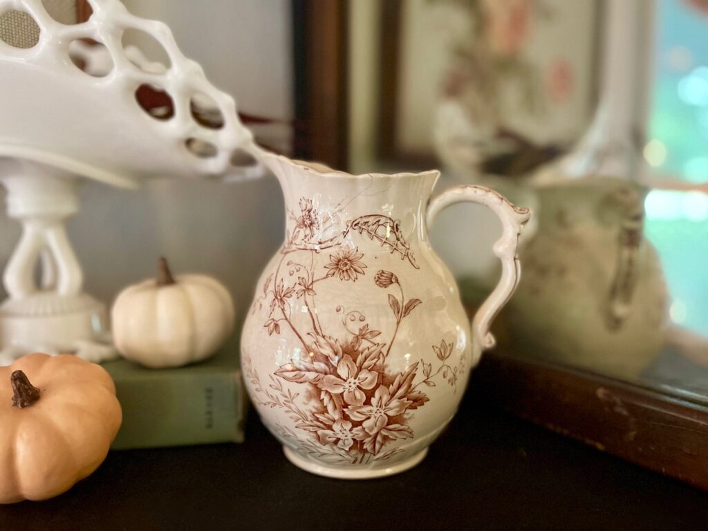 an antique transferware pitcher displayed on a mantel with some pumpkins