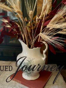 an antique pitcher filled with faux wheat stems and eucalyptus for fall