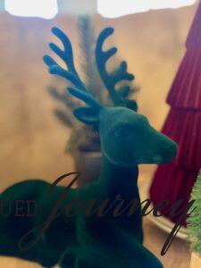 a green velvet reindeer sitting on a wood round for a Christmas display