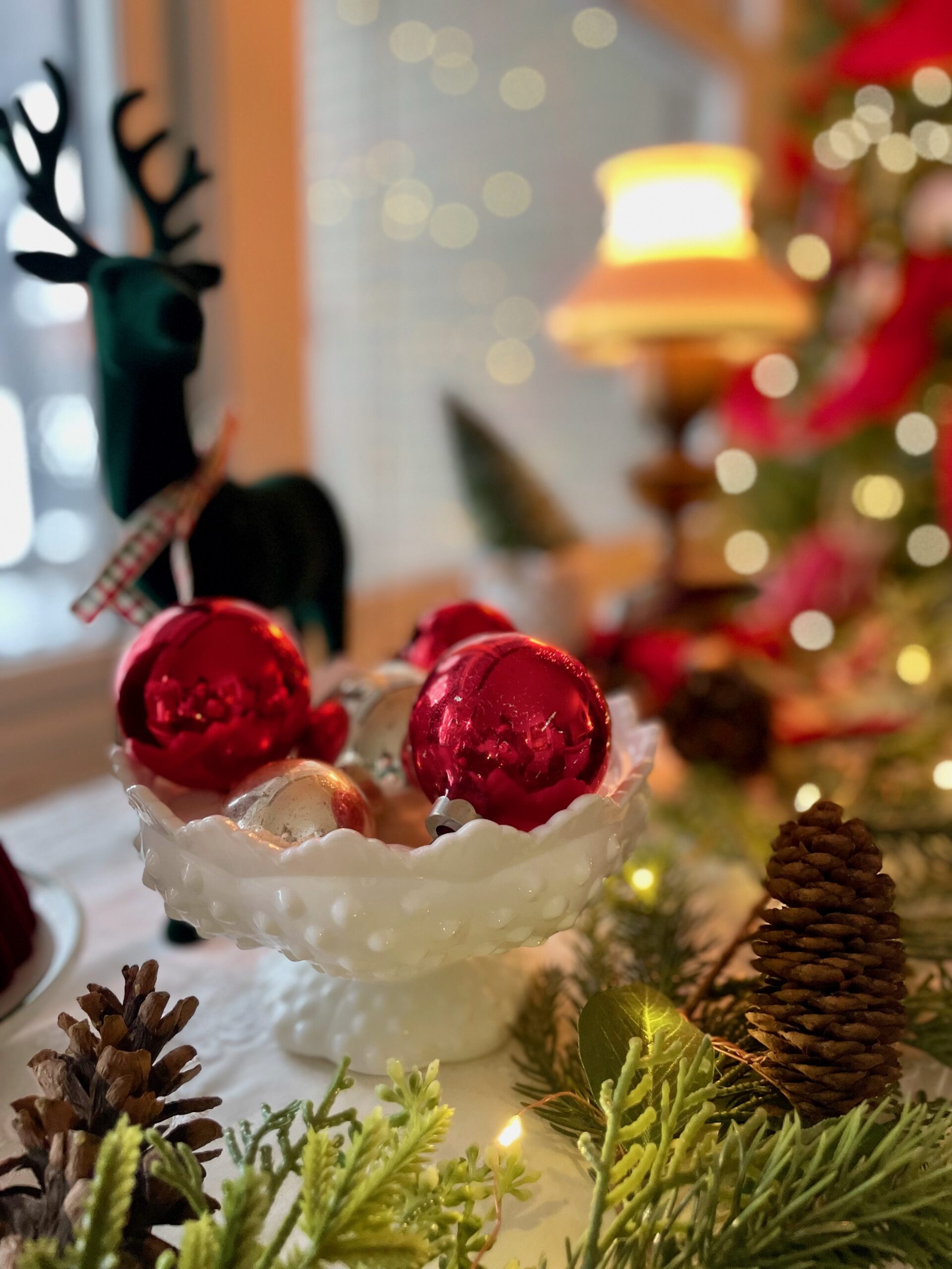 vintage Christmas ornaments in a milk glass bowl with lit garland