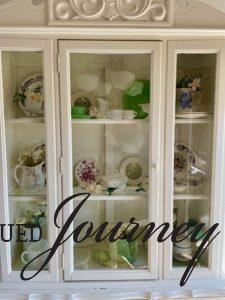 a white hutch decorated for Spring with vintage dishes