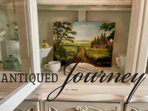 a vintage barn painting in a hutch with vintage dishes