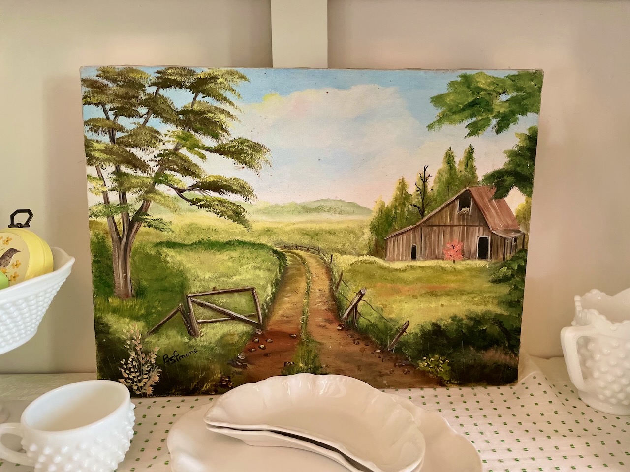 a vintage thrifted barn oil painting displayed in a hutch
