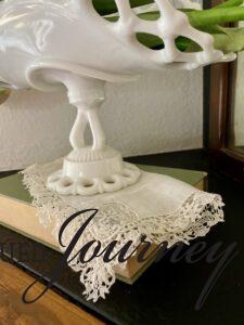 a vintage lace hanky draped over a vintage book with milk glass on a mantel