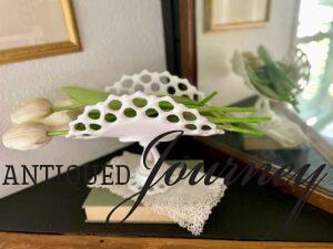 a vintage lace hanky draped over a vintage book with milk glass. How to use vintage handkerchiefs as decor.