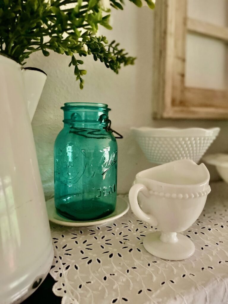 a vintage blue jar amongst vintage milk glass on a shelf