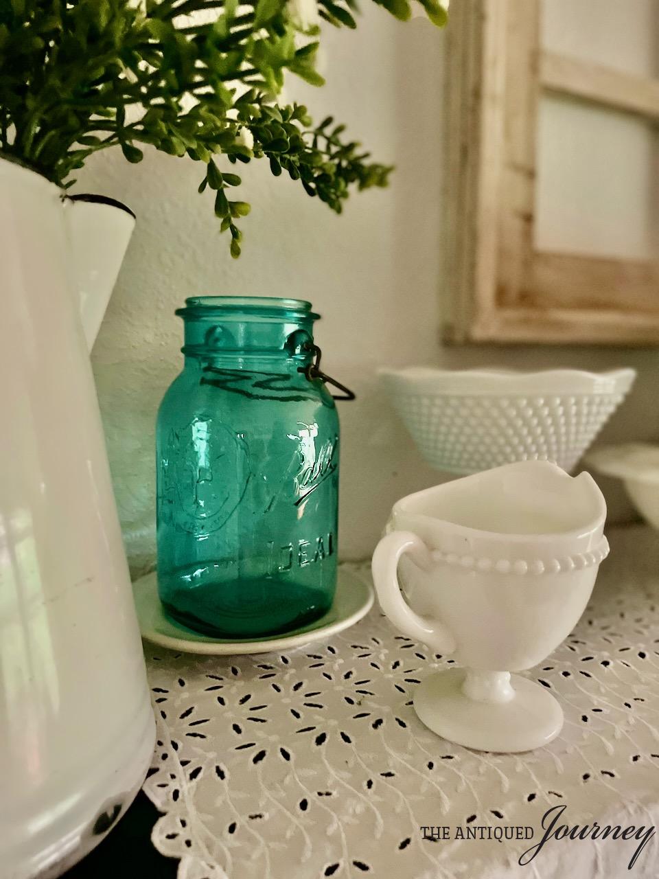 a vintage blue jar amongst vintage milk glass on a shelf