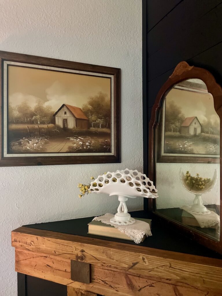 an early fall mantel display with milk glass and a vintage barn painting