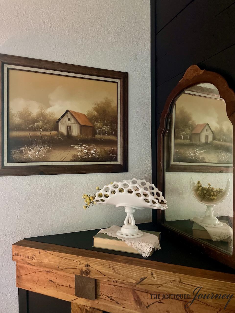 an early fall mantel display with milk glass and a vintage barn painting