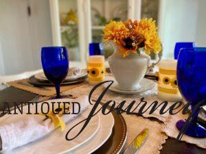 a sunflower themed table scape with blue goblets and thrifted items